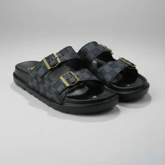 Black sandals with gold buckles on a gray background