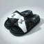 Black and white slide sandals with a brand logo on a gray background