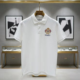 White polo shirt with a brand logo on a hanger against a gray wall with abstract art.