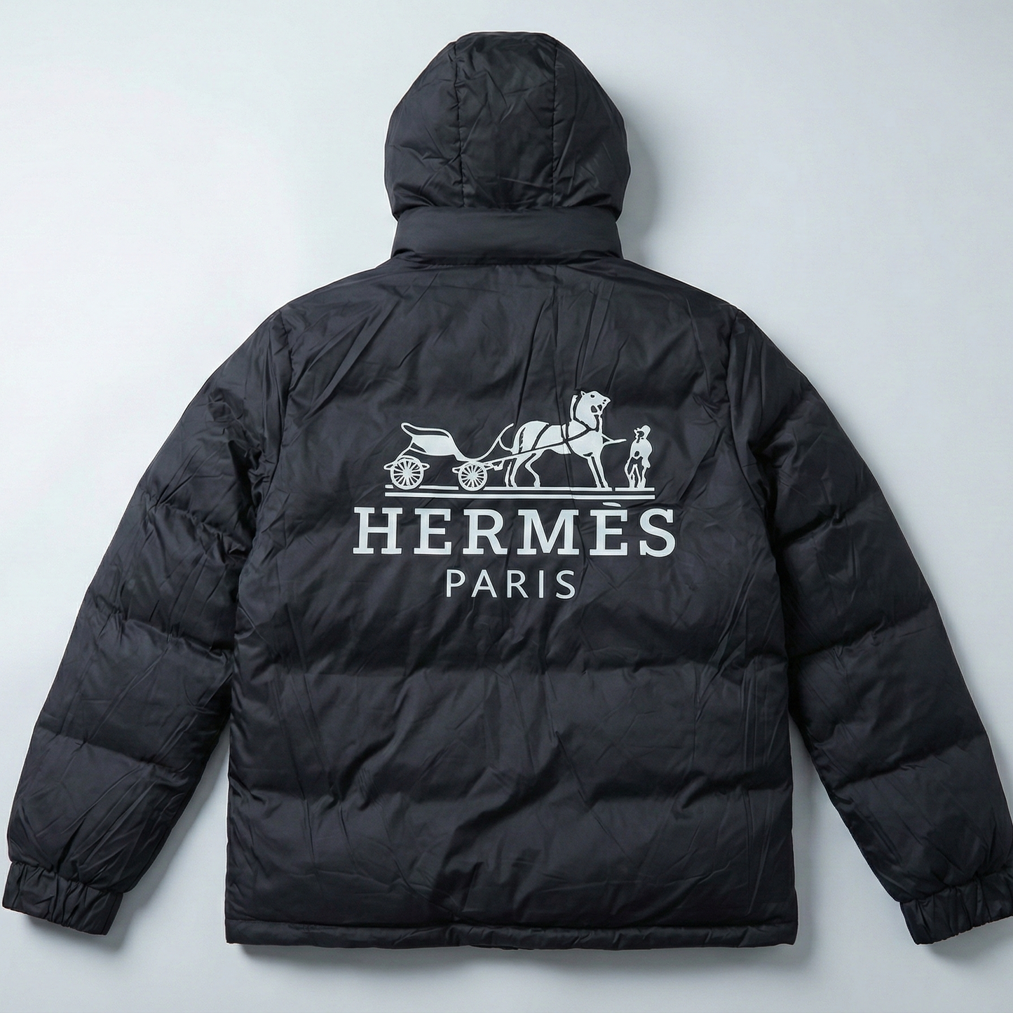 Black puffer jacket with Hermes Paris logo on a light gray background
