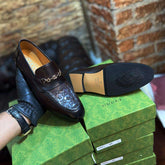 Black Gucci loafer on a stack of green Gucci boxes against a brick wall.