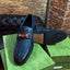 Blue leather loafer with a red buckle on a green Gucci box against a brick wall.