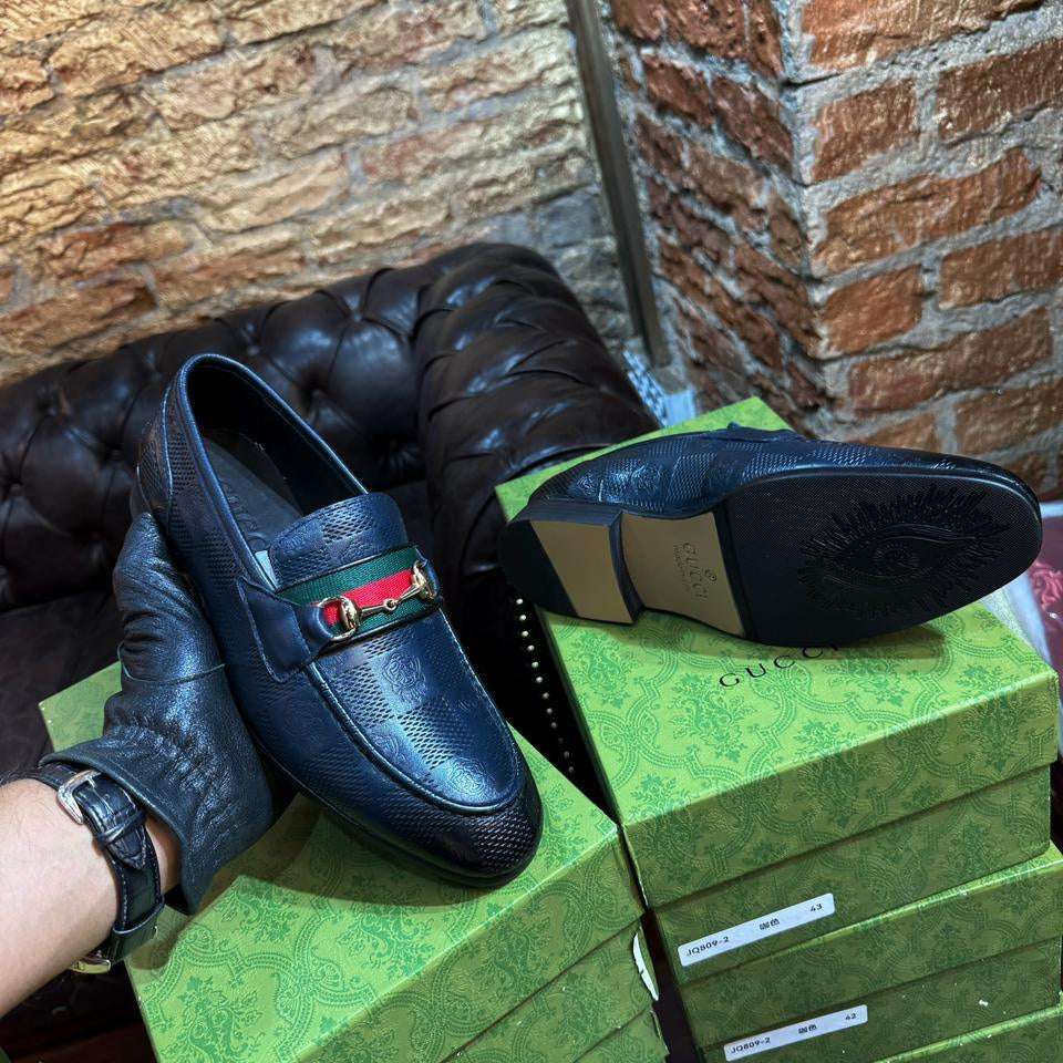 Blue loafers with a green and red detail on a stack of green boxes against a brick wall.