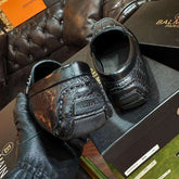 Black leather shoes on a box with Balmain branding, held by a gloved hand.