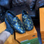 Blue loafers with a pattern on an orange shoe box, with a black leather sofa and boxes in the background.
