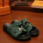 Green sandals with gold H-buckles on a wooden surface, with Hermes packaging in the background.