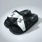 Black and white slide sandals with a brand logo on a gray background