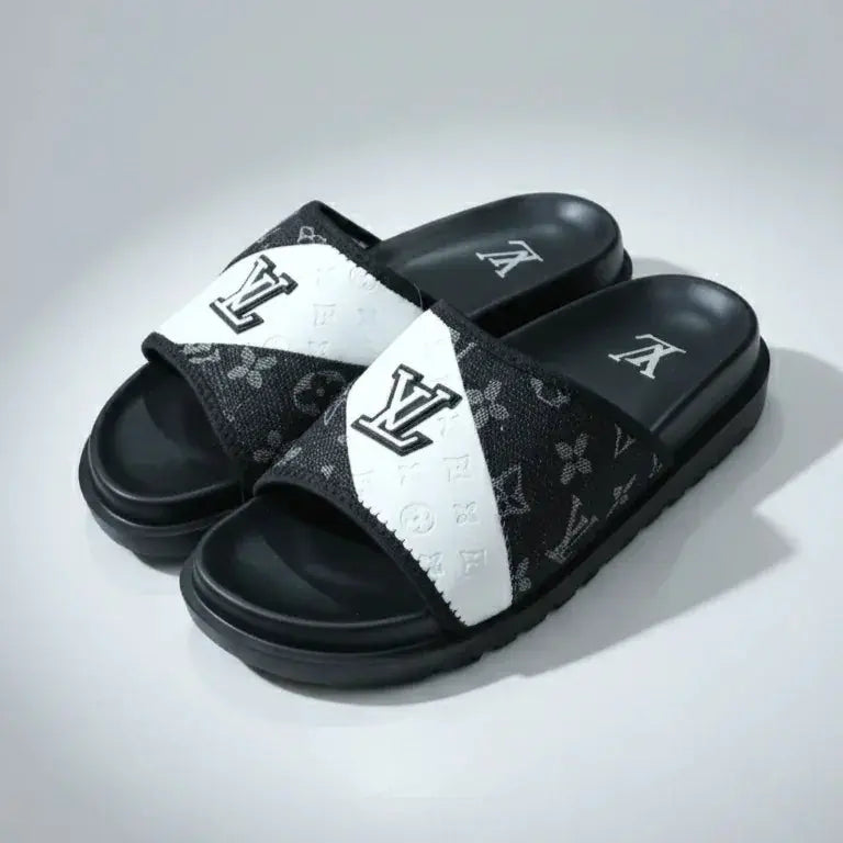 Black and white slide sandals with a brand logo on a gray background