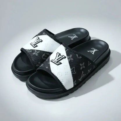 Black and white slide sandals with a brand logo on a gray background
