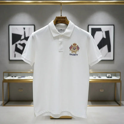 White polo shirt with a brand logo on a hanger against a gray wall with abstract art.