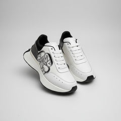 White sneakers with black accents held by a gloved hand, with Alexander McQueen boxes in the background.