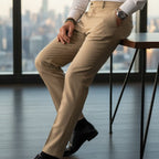 Man in a white shirt and beige pants sitting in an office with a cityscape view.