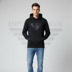 Man wearing a black Emporio Armani hoodie and blue jeans on a gray background