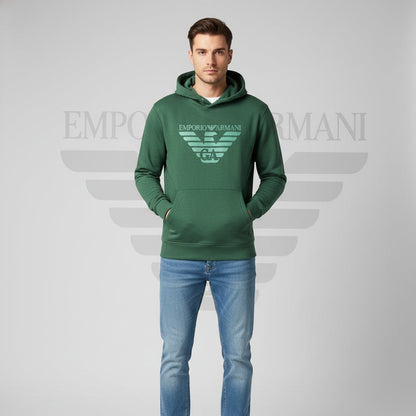 Man wearing a green Emporio Armani hoodie and blue jeans on a gray background