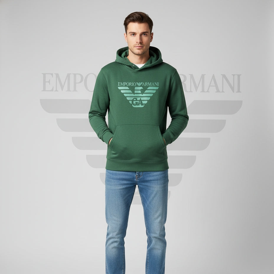 Man wearing a green Emporio Armani hoodie and blue jeans on a gray background