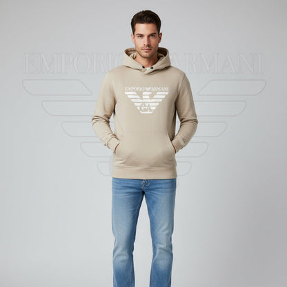 Man wearing a beige Emporio Armani hoodie and blue jeans on a gray background