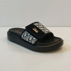 Black slide sandal with floral design and brand logo on a white background