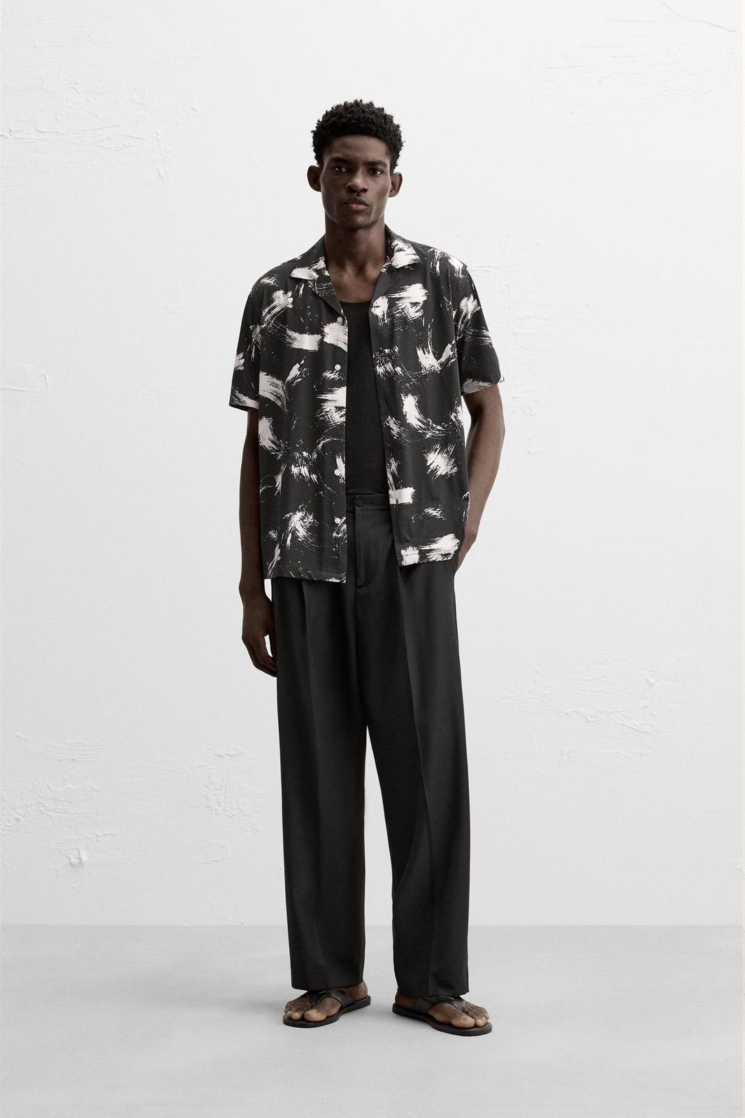 Person wearing a patterned shirt and black pants on a white background