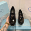 Black Prada loafers held by a hand with a tattoo, on a blue Prada box.