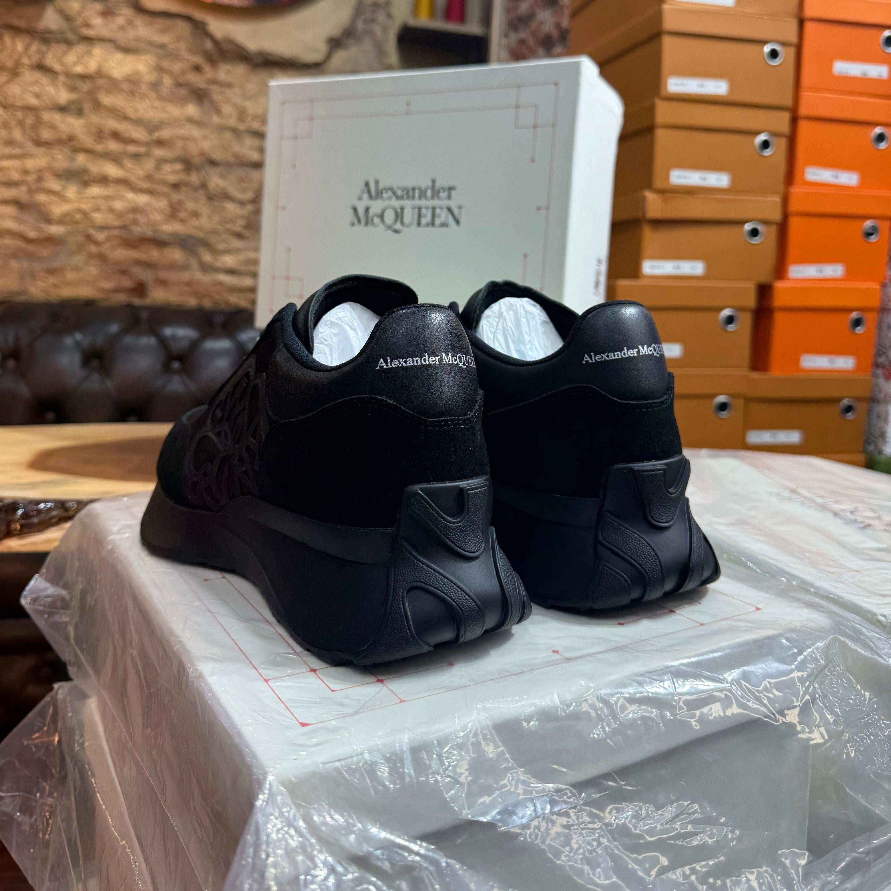 Rear view of the all-black Alexander McQueen Sprint Runner sneakers, showcasing the signature logo on the leather heel counter."