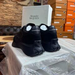 Rear view of the all-black Alexander McQueen Sprint Runner sneakers, showcasing the signature logo on the leather heel counter."