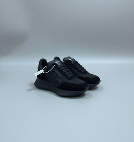 An all-black Alexander McQueen Sprint Runner sneaker being held to show its suede and leather details, embossed side logo, and thick chunky sole.