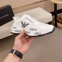 White Armani sneakers with black soles held by a hand, brand box in the background.