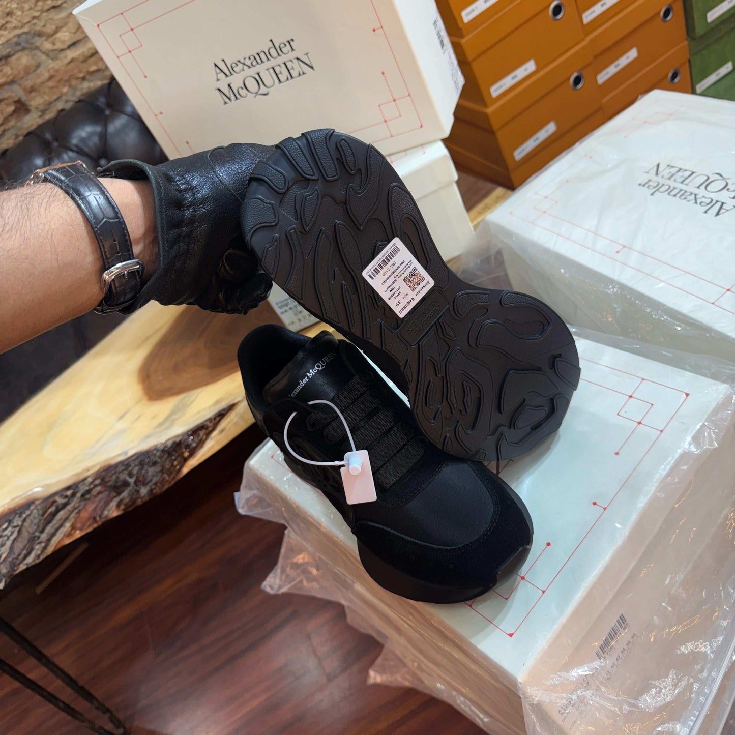 Black shoes with a tag on a white surface, next to a box labeled 'Alexander McQueen'.