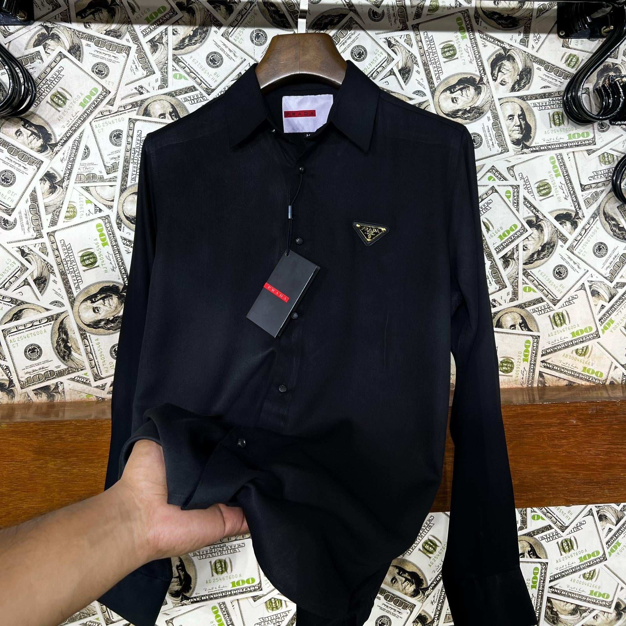 Black shirt on a hanger with a Prada tag against a background of dollar bills and 'UNIVERSES' text.