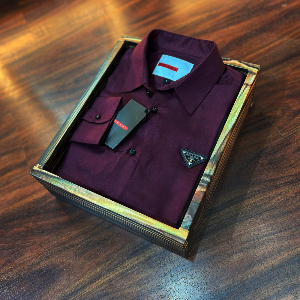 Maroon shirt with a brand logo in a wooden box on a wooden surface