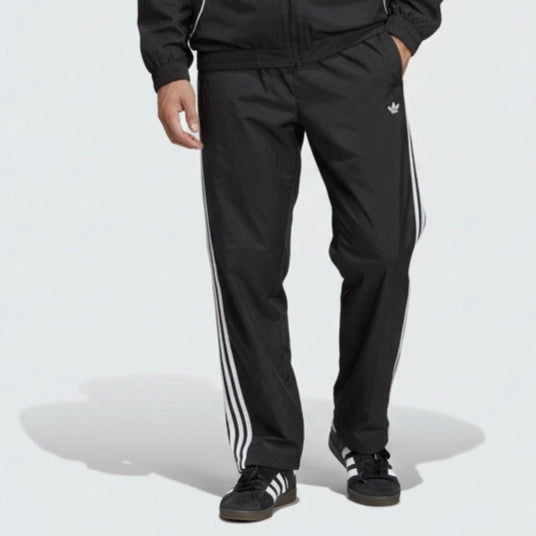 Person wearing a black Adidas tracksuit with white stripes on a light gray background