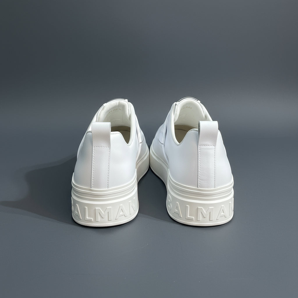 White sneakers with 'Balenciaga' branding on a white surface against a stone wall background.