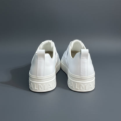 White sneakers with 'Balenciaga' branding on a white surface against a stone wall background.