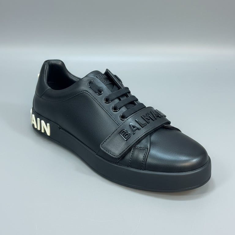 Black leather shoe with 'B MAN' branding held by a person against a dark background.