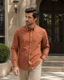 A man wearing a rust-orange long-sleeve button-down shirt by Polo Ralph Lauren and khaki pants, standing on stone steps in front of a building.