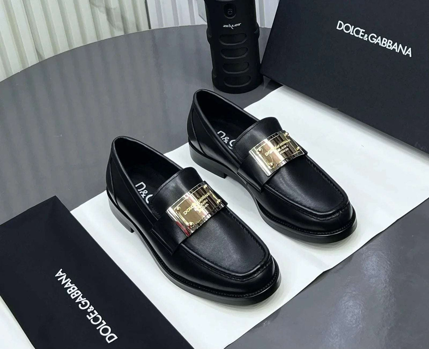 Black loafers with gold buckles on a Dolce & Gabbana branded box.
