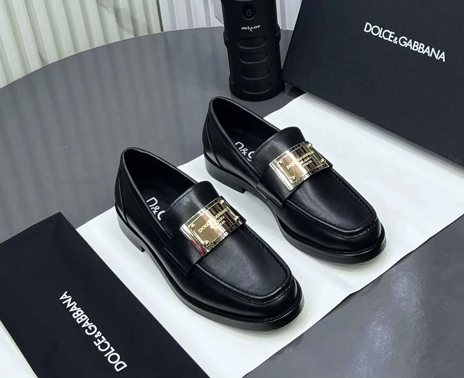 Black loafers with gold buckles on a Dolce & Gabbana branded box. Main image