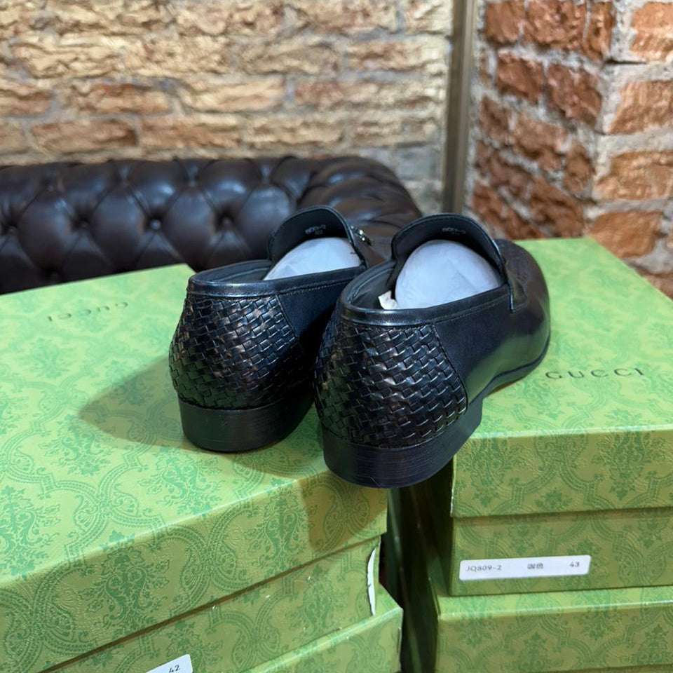 Black shoes on a green Gucci box with a brick wall background