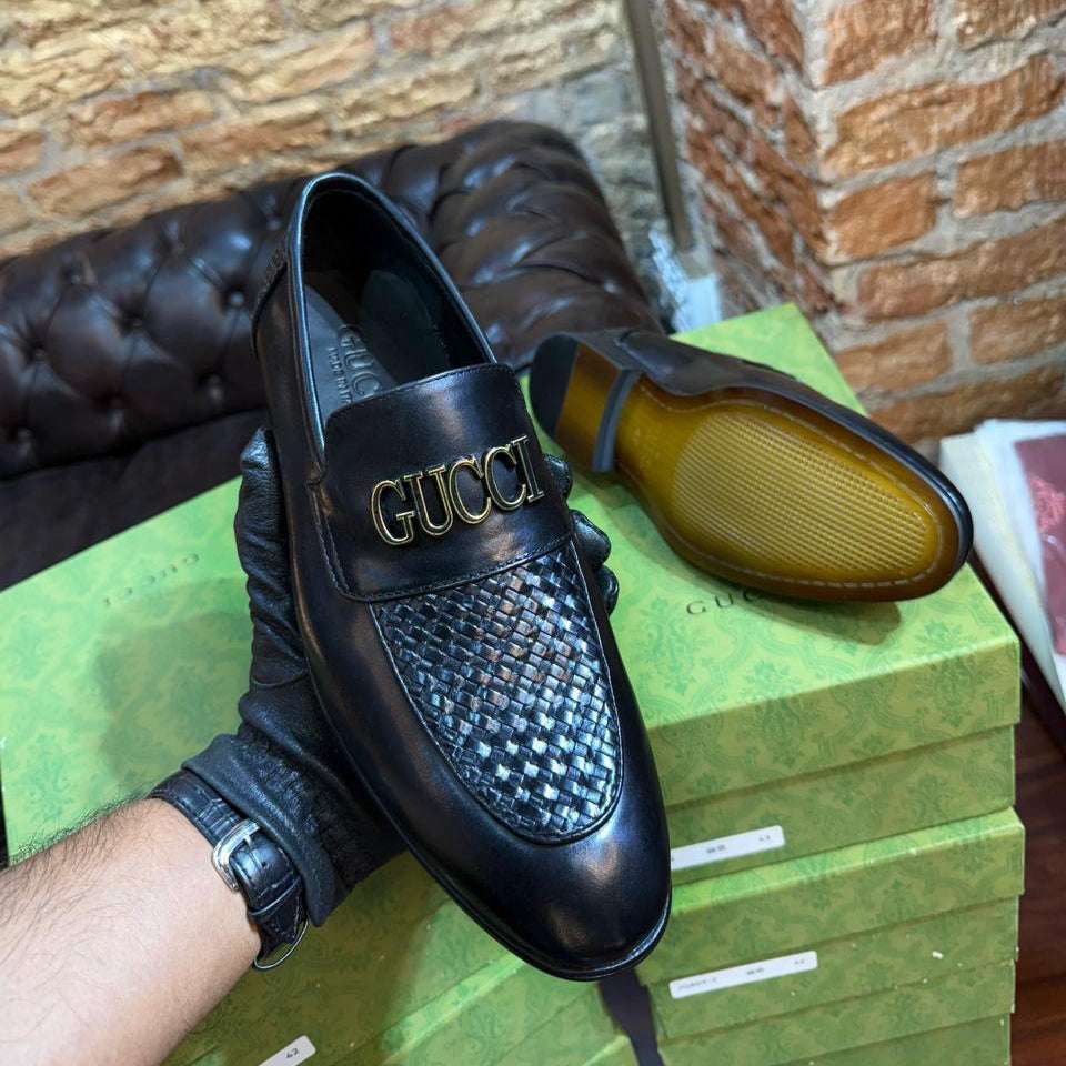 Black Gucci loafer on a green box with a brick wall background
