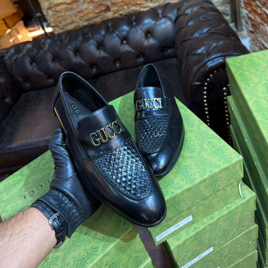 Black Gucci loafers on a green box with a stone wall background