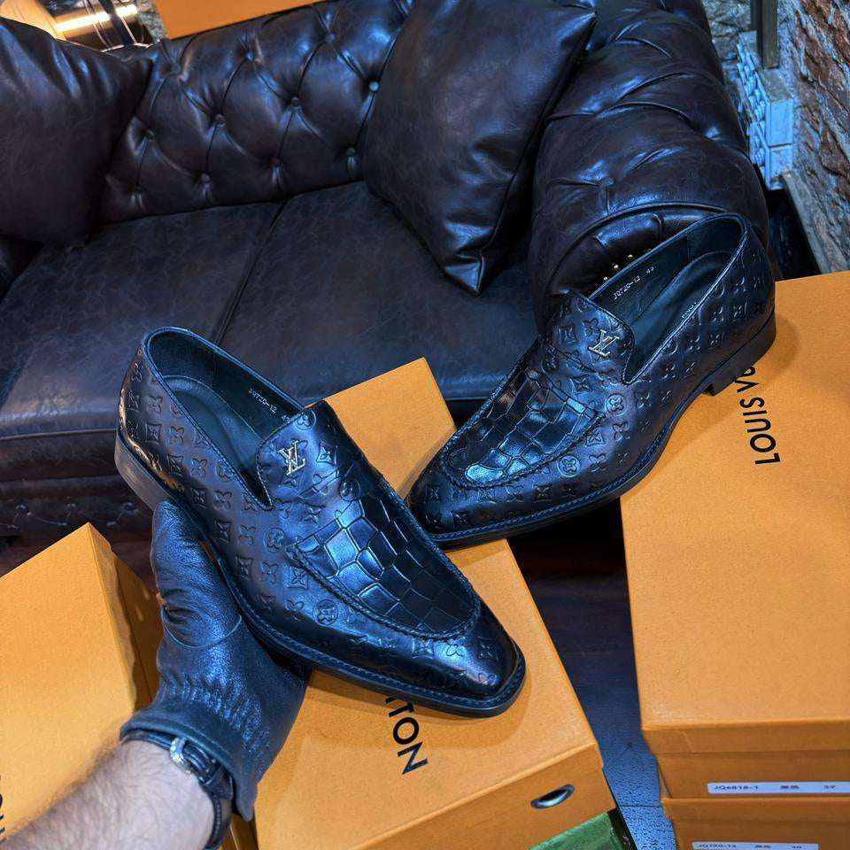 Black leather shoes on a Louis Vuitton box with a black leather couch and boxes in the background.