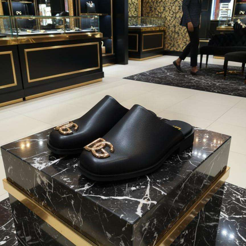 Black clogs with gold logo on a black marble platform in a luxurious store setting.