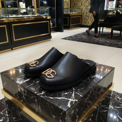 Black clogs with gold logo on a black marble platform in a luxurious store setting.