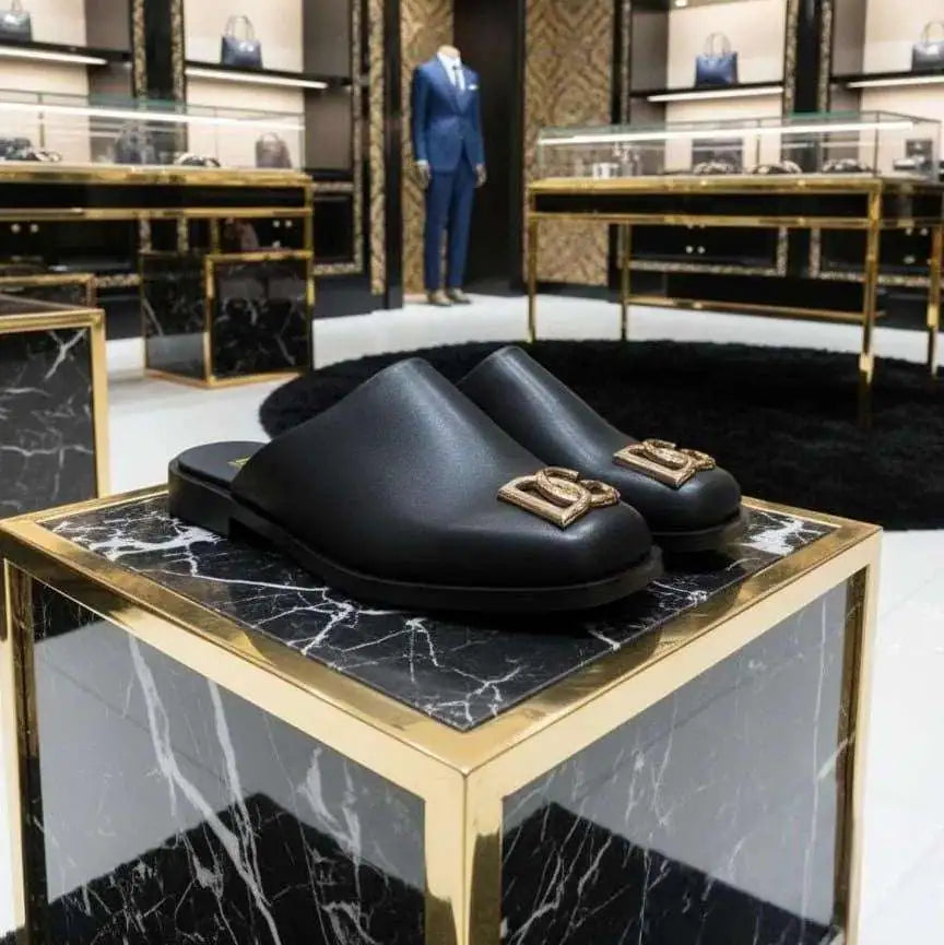 Black loafers with gold accents on a marble and gold display table in a high-end store setting.