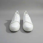 White sneakers with a logo on a wooden surface next to a laptop.