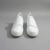 White sneakers with a logo on a wooden surface next to a laptop.
