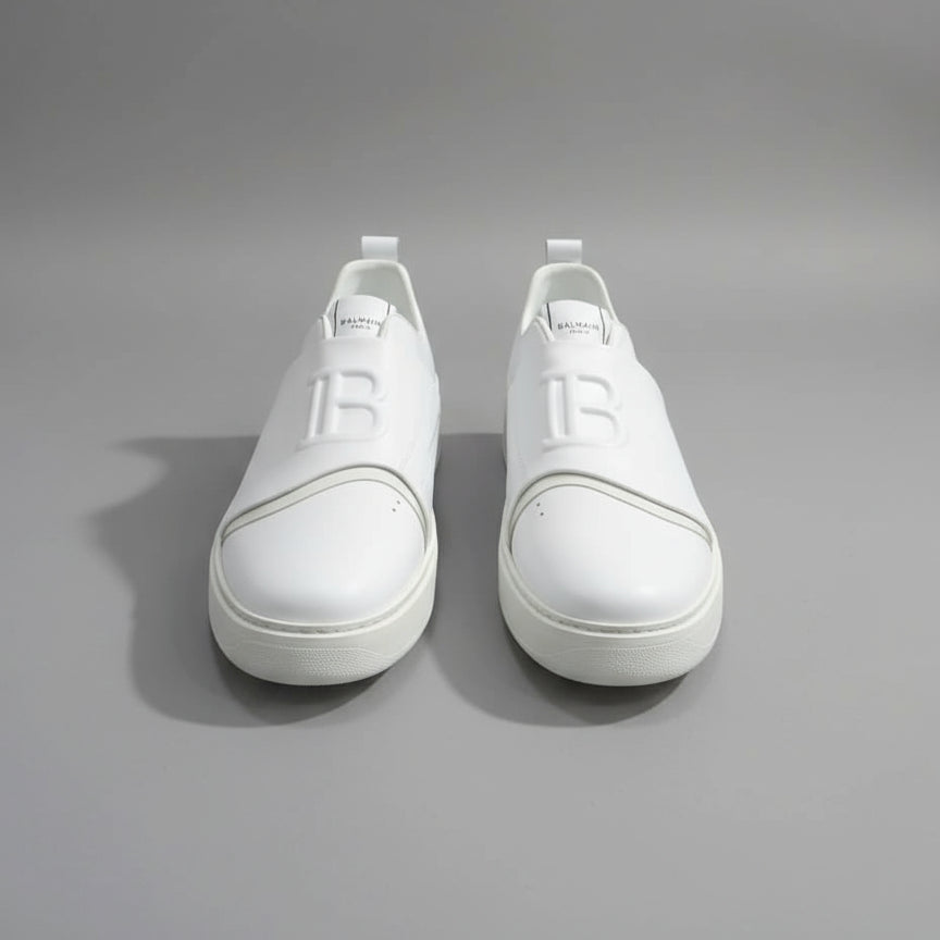 White sneakers with a logo on a wooden surface next to a laptop.