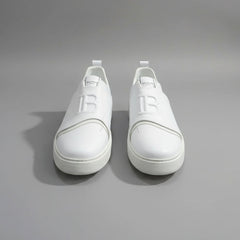 White sneakers with a logo on a wooden surface next to a laptop.