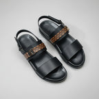 Black sandals with brown strap on a wooden surface