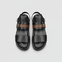 Black sandals with patterned straps on a wooden surface